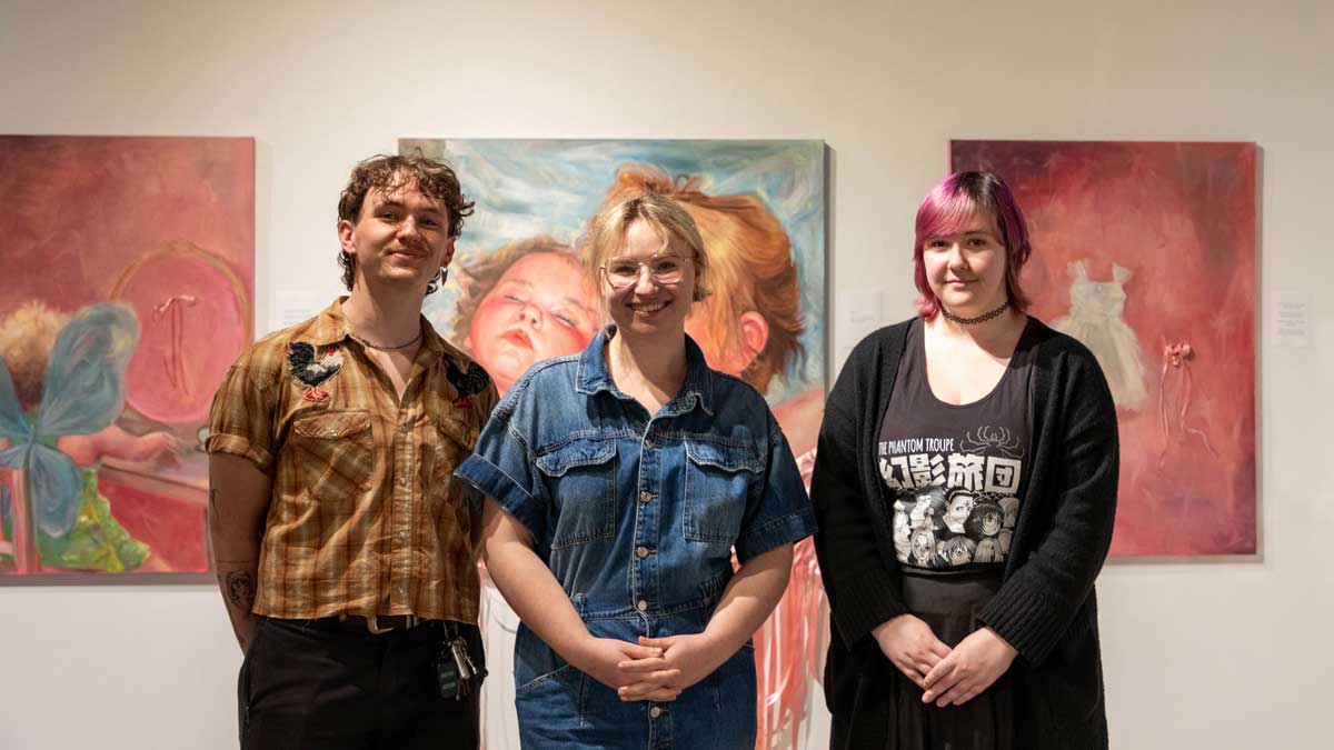 Three people are standing in front of artwork hanging on a wall